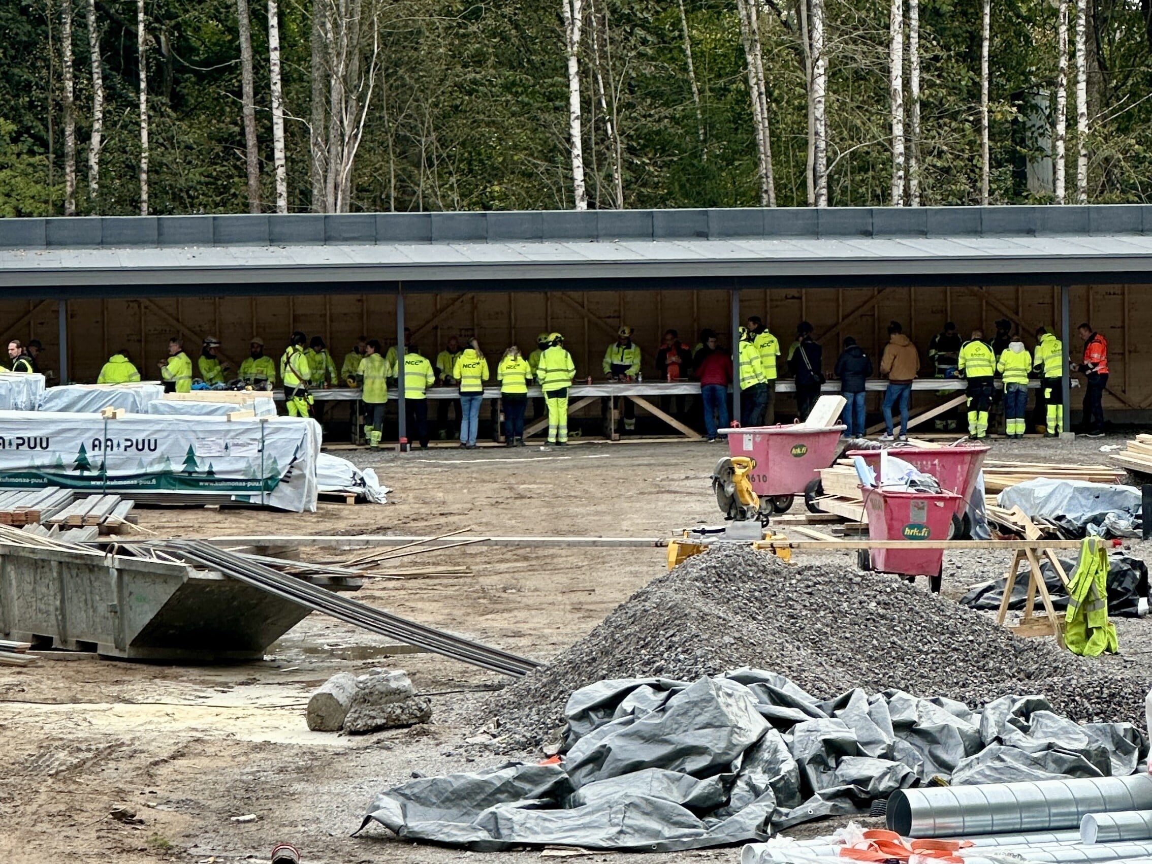 Ihmiset kokoontuivat autokatokseen nauttimaan tarjolla olevista ruuista. Kuvassa näkyy osa rakennustyömaata.